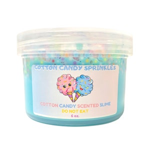 May include: A clear plastic container filled with blue slime with colorful sprinkles. The container has a white label that says "Cotton Candy Sprinkles" and "Cotton Candy Scented Slime Do Not Eat 6 oz.".