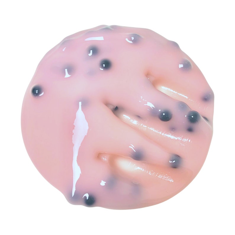 May include: A close-up of a pink, jelly-like substance with small, dark, round inclusions. The substance is spread out on a white background.