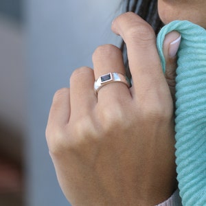 Pode incluir: Um anel de prata com uma pedra retangular azul escura engastada em um engaste de bezel.
