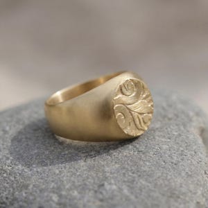 A gold ring with an embossed design rests on a gray rock.
