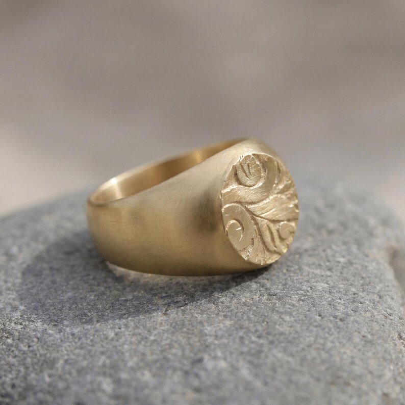A gold ring with an embossed design rests on a gray rock.