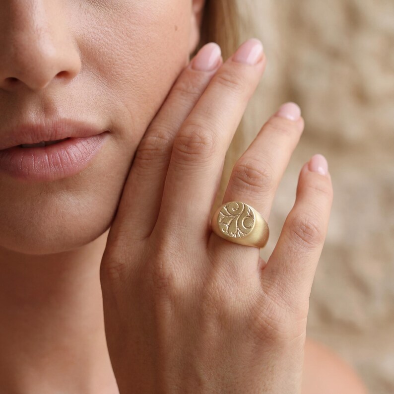 A close-up of a person's hand wearing a gold ring with an embossed design.