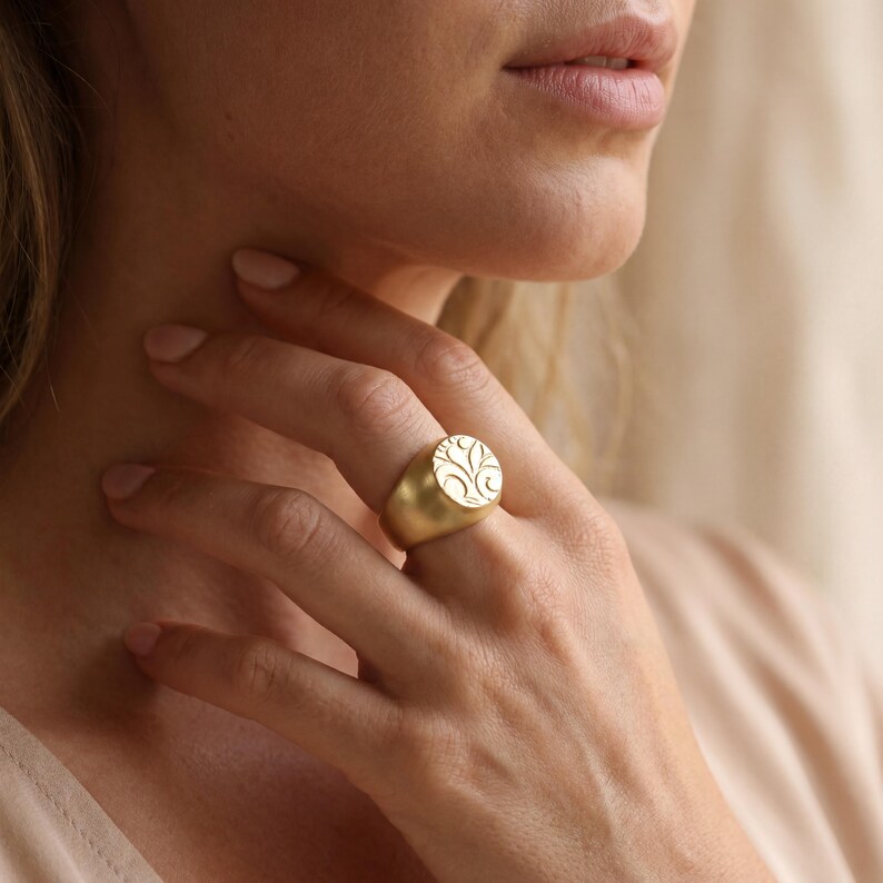 A close-up of a woman's hand wearing a gold ring with a tree-like design.