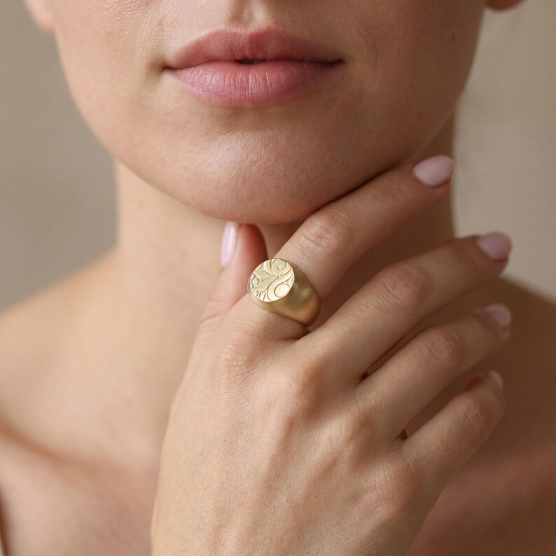 A close-up of a woman's hand wearing a gold engraved ring, with her chin resting on her hand.