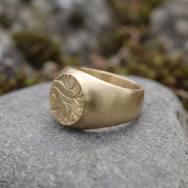 A gold ring with a leaf-like design sits on a gray rock.