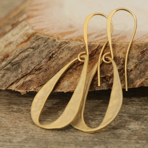 May include: A pair of gold-toned dangle earrings with a hammered finish. The earrings are oval shaped and have a simple, minimalist design.
