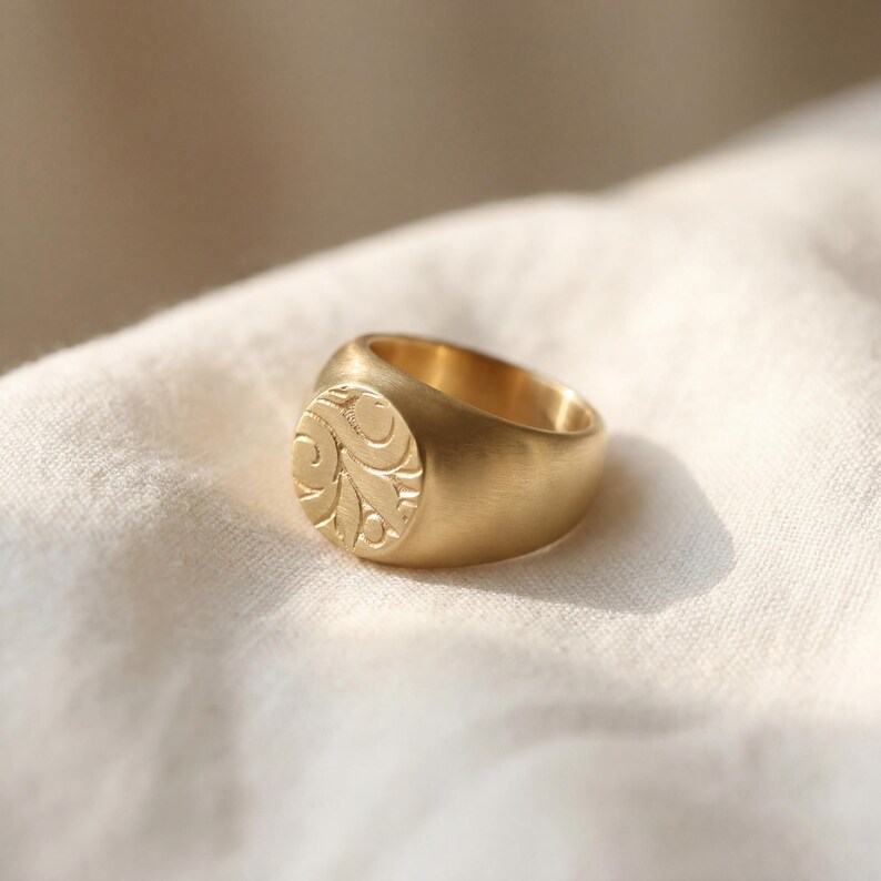 A gold ring with a decorative design sits on a white cloth.