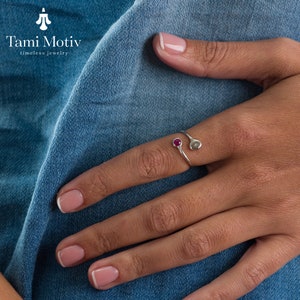 Puede incluir: Un anillo de plata con dos pequeñas piedras redondas de color rosa. El anillo está en un dedo.