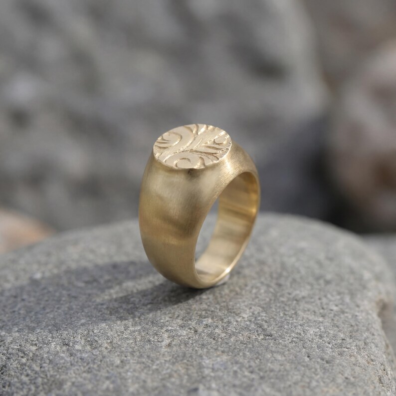 A gold ring with a circular emblem sits on a gray rock.