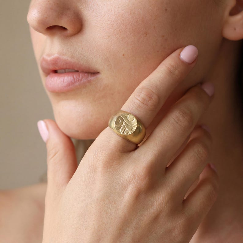 A close-up of a person's hand wearing a gold ring with an embossed design.