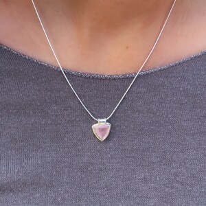 Puede incluir: Un collar de cadena de plata con un colgante triangular con una piedra preciosa rosa.