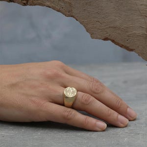 A close-up of a person's hand wearing a gold ring with a floral design.