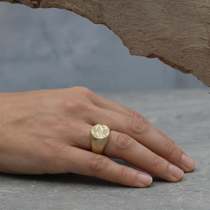 A close-up of a person's hand wearing a gold ring with a floral design.