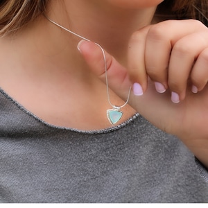 May include: A silver chain necklace with a triangular pendant featuring a light blue gemstone.