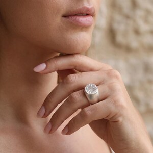 A close-up of a person's hand wearing a silver ring, with their chin resting on their hand.