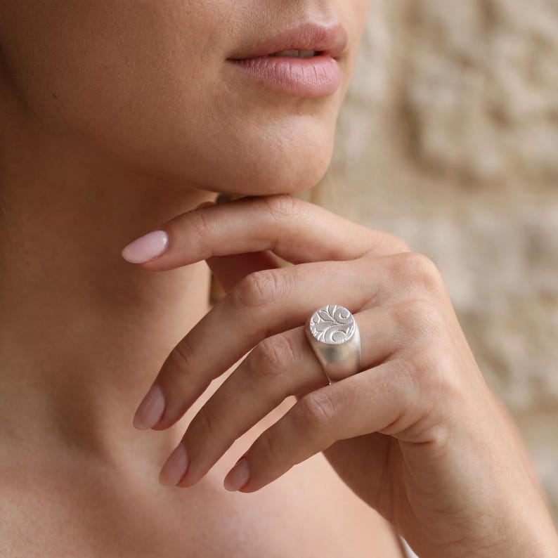A close-up of a person's hand wearing a silver ring, with their chin resting on their hand.