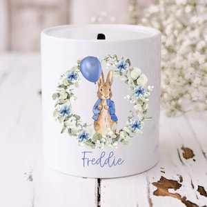 May include: A white ceramic mug with a black handle and the text "But first, coffee" in a handwritten style. The mug is on a white surface. The mug is 10 cm tall.
