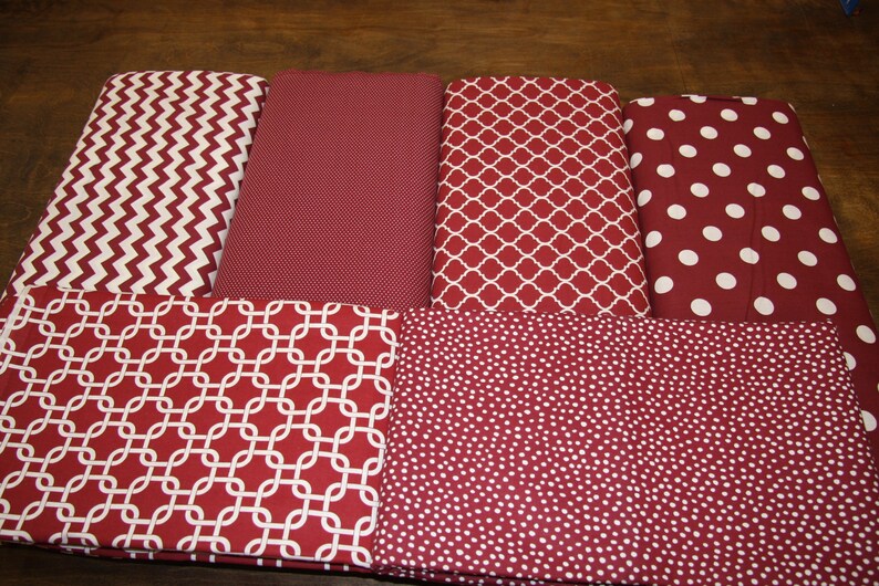 May include: Assortment of fabric pieces in various patterns, including chevron, solid, quatrefoil, and polka dots. The fabrics are primarily burgundy with white accents, suitable for crafting or home decor projects.