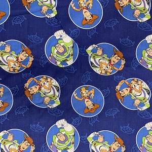 Puede incluir: Tela azul con un patrón repetido de círculos blancos que presentan imágenes de dibujos animados de Buzz Lightyear y Woody de la franquicia Toy Story. Los personajes se representan en una pose juguetona y dinámica.