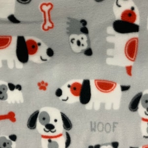 May include: A light gray fabric with a repeating pattern of cartoon dogs in white, black, and red. The word "WOOF" is printed in gray. The design includes dog bones and paw prints.