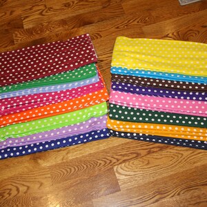 May include: Stacks of fabric in various colors, each with a white polka dot pattern. Colors include burgundy, green, blue, pink, orange, lime green, purple, and navy. The other stack includes yellow, brown, purple, pink, dark green, and orange.