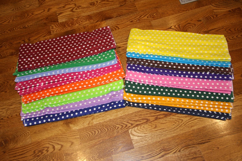 May include: Stacks of fabric in various colors, each with a white polka dot pattern. Colors include burgundy, green, blue, pink, orange, lime green, purple, and navy. The other stack includes yellow, brown, purple, pink, dark green, and orange.