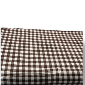 Pode incluir: Tecido xadrez marrom e branco. O tecido apresenta um padrão xadrez clássico, com quadrados marrons e brancos espaçados uniformemente. O tecido está dobrado, revelando a textura e o padrão. Adequado para projetos de costura e artesanato.