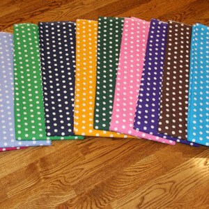 May include: A collection of colorful fabric squares, each featuring a polka dot pattern. The squares are arranged in a semi-circle, showcasing a variety of colors including purple, green, orange, pink, blue, and yellow. The polka dots are white.
