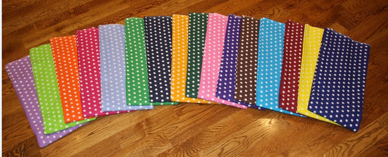May include: A collection of colorful fabric squares, each featuring a polka dot pattern. The squares are arranged in a semi-circle, showcasing a variety of colors including purple, green, orange, pink, blue, and yellow. The polka dots are white.