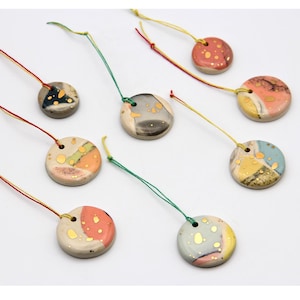 May include: Nine round ceramic ornaments with colorful abstract patterns and gold accents. Each ornament has a hole at the top for hanging with a string.
