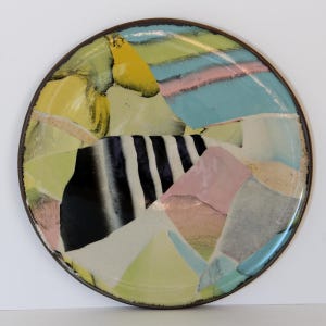 May include: A round ceramic plate with a colorful abstract design. The plate features a dark brown rim and a vibrant pattern of yellow, black, pink, blue, and white shapes. The design includes vertical black and white stripes. A unique piece for serving or display.