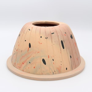 May include: A ceramic dome-shaped planter with a wide base and a textured, ribbed surface. The planter is decorated with a marbled pattern in shades of peach, orange, and grey, with black splatter paint accents.