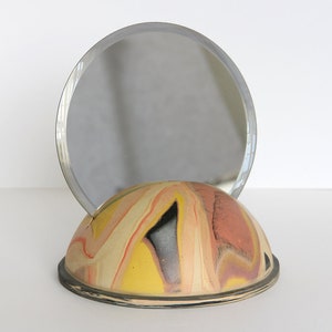Peut inclure: Un socle rond en céramique marbrée jaune, rose et noir avec un miroir rond à cadre argenté sur le dessus.