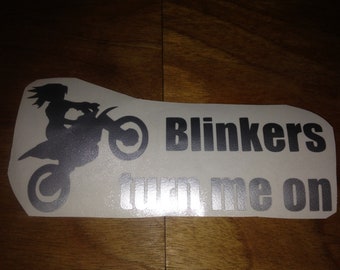May include: A black and white sticker with a silhouette of a person riding a dirt bike. The text "Blinkers turn me on" is written below the image.