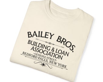 May include: A white t-shirt with a black graphic print that reads "BAILEY BROS. EST. 1909 BUILDING & LOAN ASSOCIATION GENESEE STREET. BEDFORD FALLS, NEW YORK"