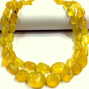 May include: A strand of yellow gemstone beads, likely opal, in a teardrop shape. The beads are strung on a clear thread and are arranged in a double row.