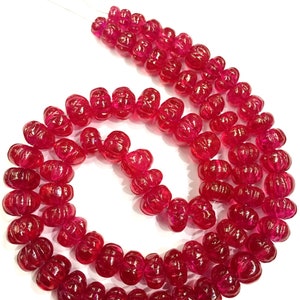 May include: A strand of bright red faceted gemstone beads. The beads are carved with a flower design and are strung on a thin wire.