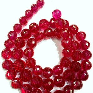 Op de afbeelding: Een streng facetgeslepen robijnrode edelsteen kralen. De kralen zijn rond en hebben een gepolijste afwerking.