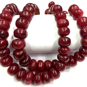 Op de afbeelding: Twee strengen gepolijste, dieprode edelsteen kralen. De kralen zijn rond en tonvormig, geregen tot kettingen. De kleur is een rijk, donkerrood met een glanzende afwerking, wat wijst op een natuurlijk steenmateriaal.