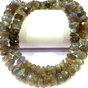 以下が含まれることがあります： 虹色の緑色のラブラドライトの宝石ビーズのストランド。ビーズはファセットカットされており、わずかに不規則な形をしています。ビーズは透明な糸に糸で通されています。