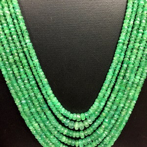 K&ouml;nnte beinhalten: Eine mehrstr&auml;ngige Halskette aus kleinen, facettierten Smaragdperlen. Die Halskette hat eine leuchtend gr&uuml;ne Farbe und wird vor einem dunklen Hintergrund pr&auml;sentiert. Die Str&auml;nge fallen in einer anmutigen, geschichteten Anordnung, die den Glanz des Edelsteins zeigt.