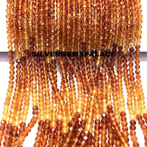 May include: Multiple strands of faceted, round, translucent orange and deep amber beads arranged in vertical rows. The text SILVERGEMSPALACE is printed in black across the center of the beads. The beads exhibit a reflective, polished surface.