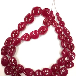 May include: A strand of deep red gemstone beads, each bead is a smooth, rounded oval shape. The beads are strung on a thin wire and are ready to be used for jewelry making.