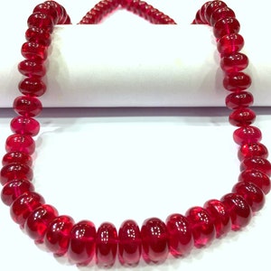 May include: A strand of deep red ruby beads, each bead is round and polished, creating a smooth and lustrous finish. The beads are strung together on a clear thread, forming a necklace.