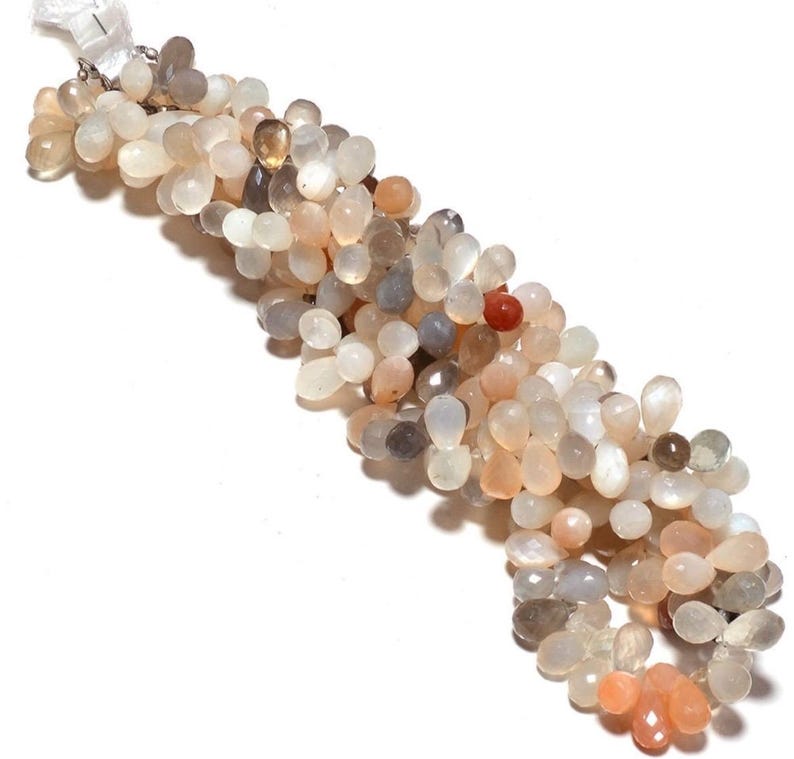 May include: A strand of light gray, peach, and white moonstone beads. The beads are teardrop shaped and have a pearlescent sheen.