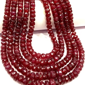 Può includere: Una collana di perle di rubino rosso scuro, sfaccettate e lucidate. Le perle sono tutte di dimensioni e forma approssimativamente uguali e hanno una finitura liscia e lucida.