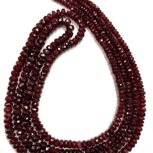 Peut inclure: Un collier à plusieurs rangs composé de pierres précieuses rouge foncé à facettes. Les perles sont enfilées ensemble, créant un effet de superposition. Le collier a un pompon en haut, ajoutant un élément décoratif. Les pierres ont une surface polie et réfléchissante.
