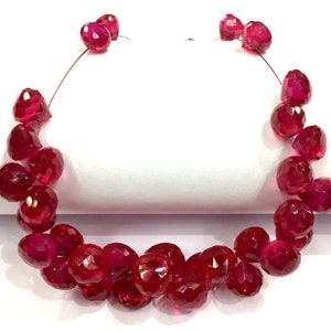 May include: A strand of ruby red faceted gemstone beads. The beads are strung on a clear thread and are arranged in a circular pattern.