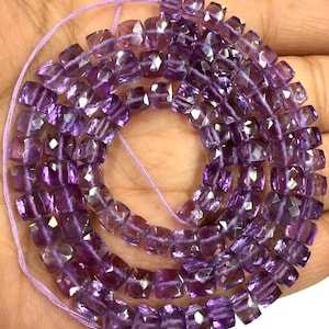 May include: A strand of purple amethyst gemstone beads, each bead is faceted and square shaped. The beads are strung on a thin purple thread.