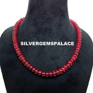 May include: A red gemstone bead necklace on a black mannequin bust. The necklace is made of round, faceted beads. The text "SILVERGEMSPALACE" is visible on the bust.